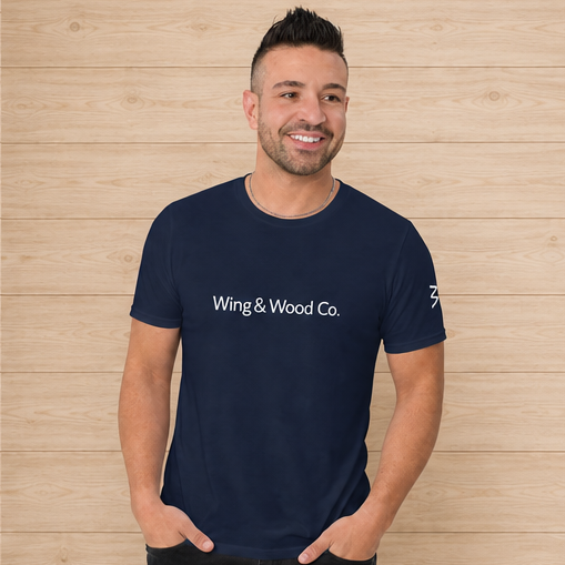 A man wearing a navy blue crewneck t-shirt with 'Wing & Wood Co.' printed in white across the chest, standing against a light wood plank wall.