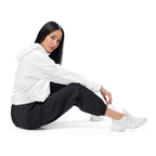 Person wearing a white wind breaker hoodie and black pants sitting on a white background