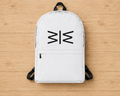 A white backpack with black straps and a black geometric logo on the front, laid flat on a light wood plank background.