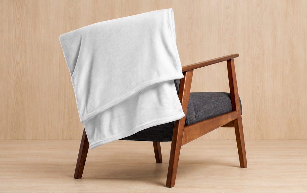 A white plush fleece throw blanket draped over a mid-century modern wooden armchair with a dark gray cushion, set against a light wood-paneled background.
