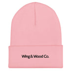 A light pink ribbed knit beanie hat with a folded cuff, featuring the black embroidered text 'Wing & Wood Co.' on the front, set against a plain white background.