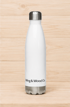 A white insulated water bottle with a silver metal cap and base, featuring the text 'Wing & Wood Co.' printed in black near the bottom, set against a light wood plank background.
