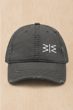 A dark gray distressed baseball cap with a white stylized 'M' logo on the front, displayed flat on a light wood background.