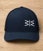 A dark navy blue trucker hat with a white stylized 'M' logo on the front, displayed flat on a light wood background.