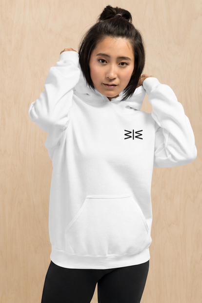 A woman wearing a white pullover hoodie with a small black geometric logo on the left chest, posed against a light wood-paneled background.