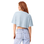 A woman with red hair is shown from the back wearing a light blue cropped t-shirt and light-wash jeans against a solid white background.