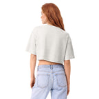 A woman with long red hair is shown from the back wearing a light gray heather cropped t-shirt and light blue jeans against a solid white background.
